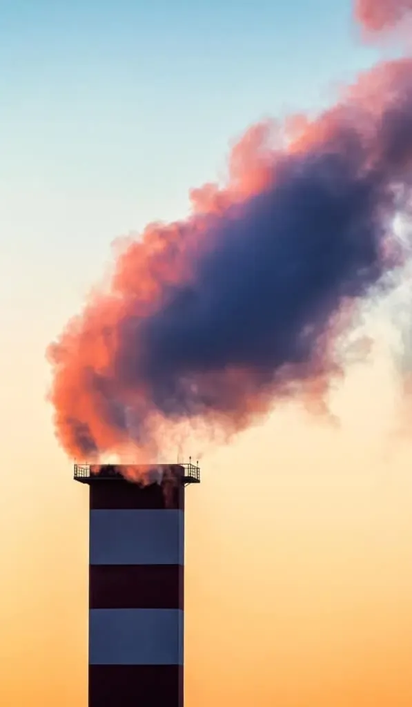 Industrial chimney emitting colorful smoke at sunset.