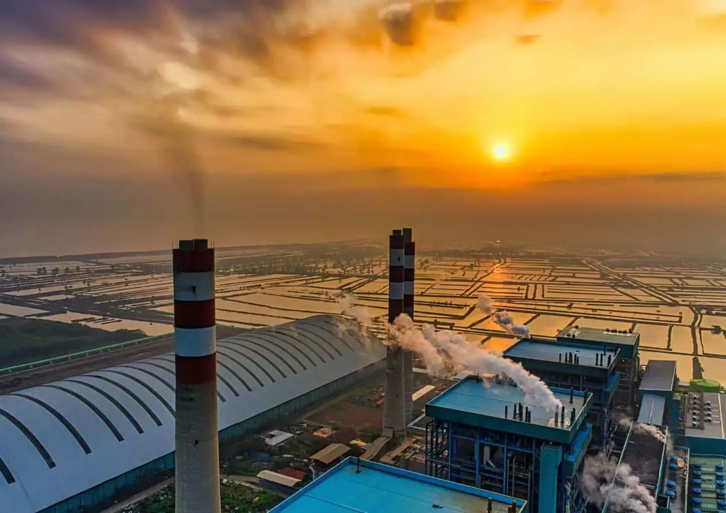 Industrial plant with smokestacks at sunset.