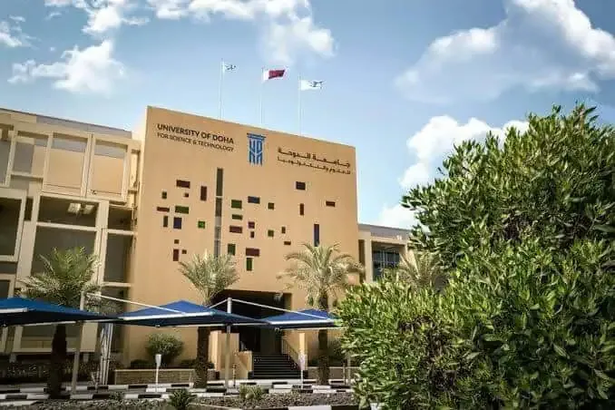 University of Doha building with trees and flags.
